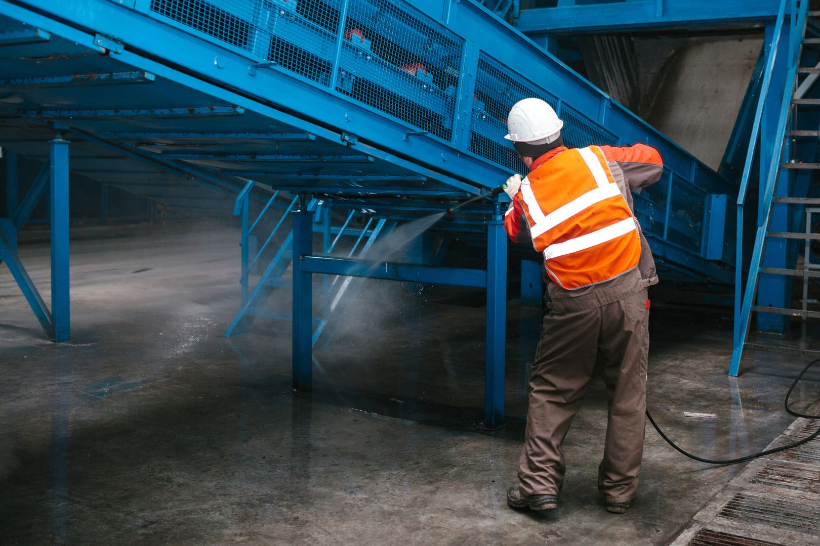 Industriereinigung mit Hochdruckreiniger: Mitarbeiter reinigt Förderanlage in Industriehalle